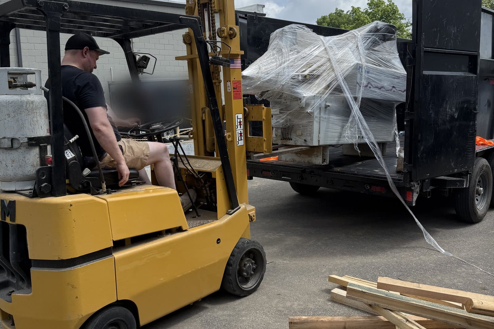 A forklift loading shrink-wrapped pallets of office equipment into a Redemption dump trailer during a commercial cleanout.