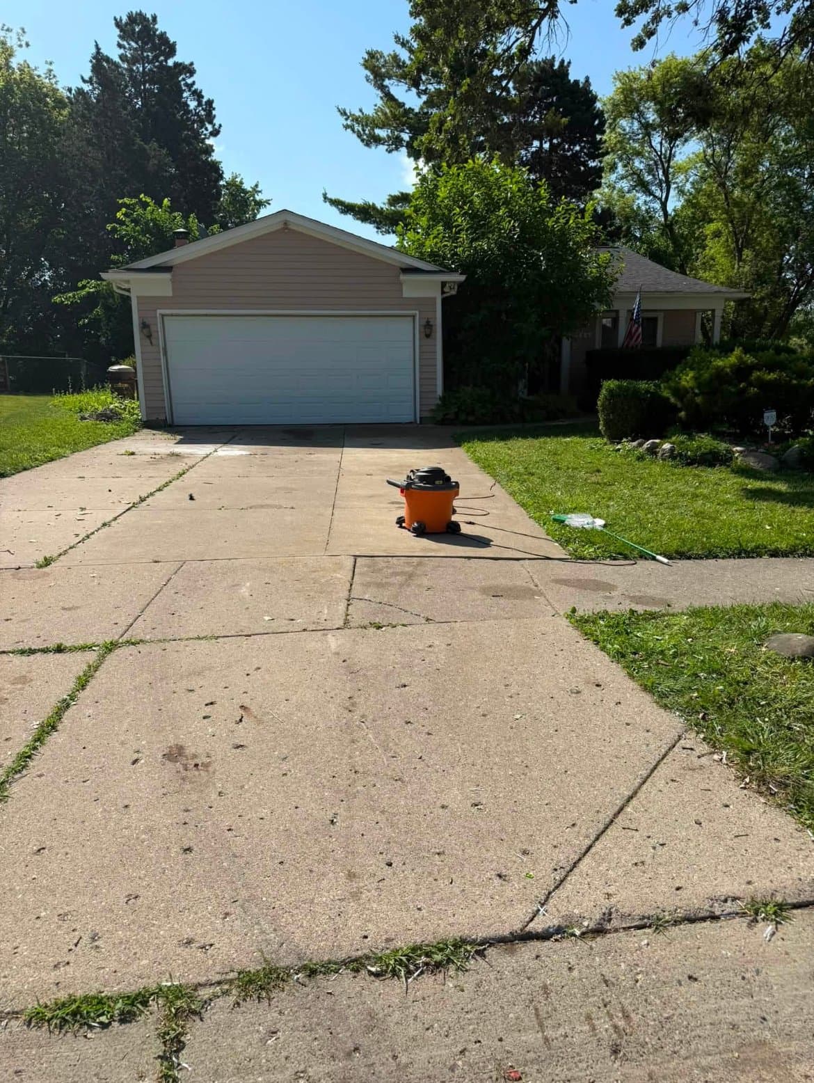 After: The same driveway and beige garage completely cleared, with only a shop vacuum left on the concrete.