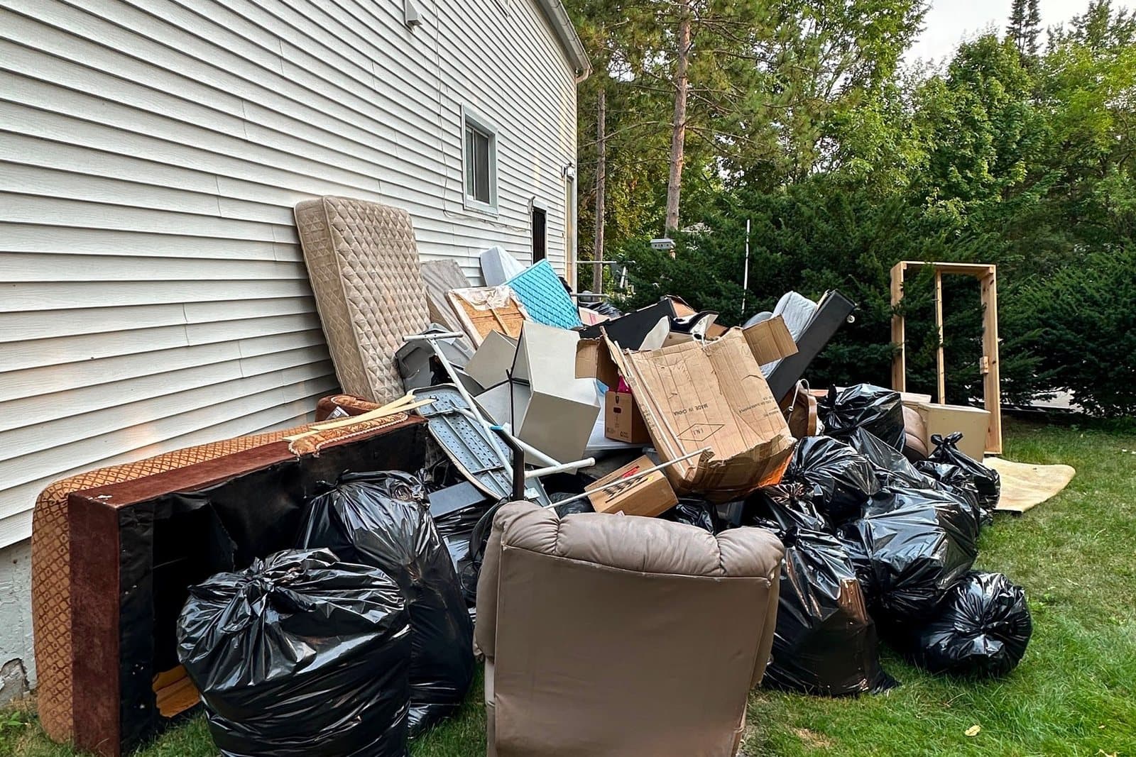 Furniture, mattresses, and bagged household contents staged for removal alongside a home during a full-property cleanout.