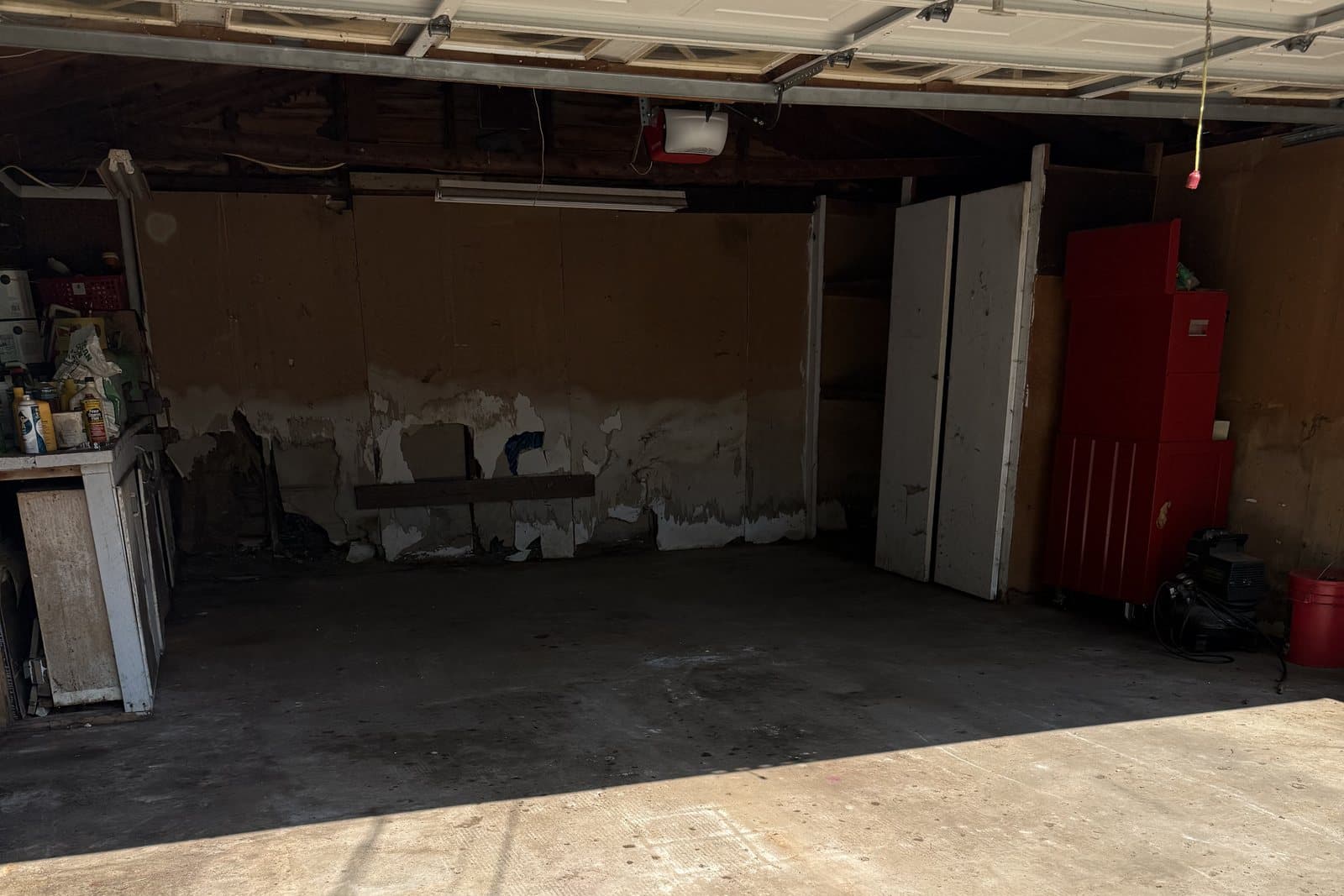 After: The same garage emptied to a bare floor, with a red tool chest, cabinets, and a shelf left in place.