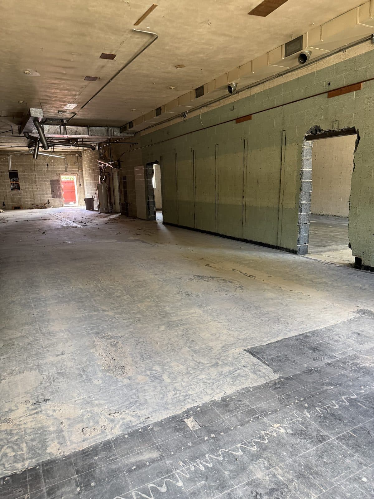 A commercial interior stripped to bare block walls and concrete slab after a full gut-out, with the framing openings left in place.