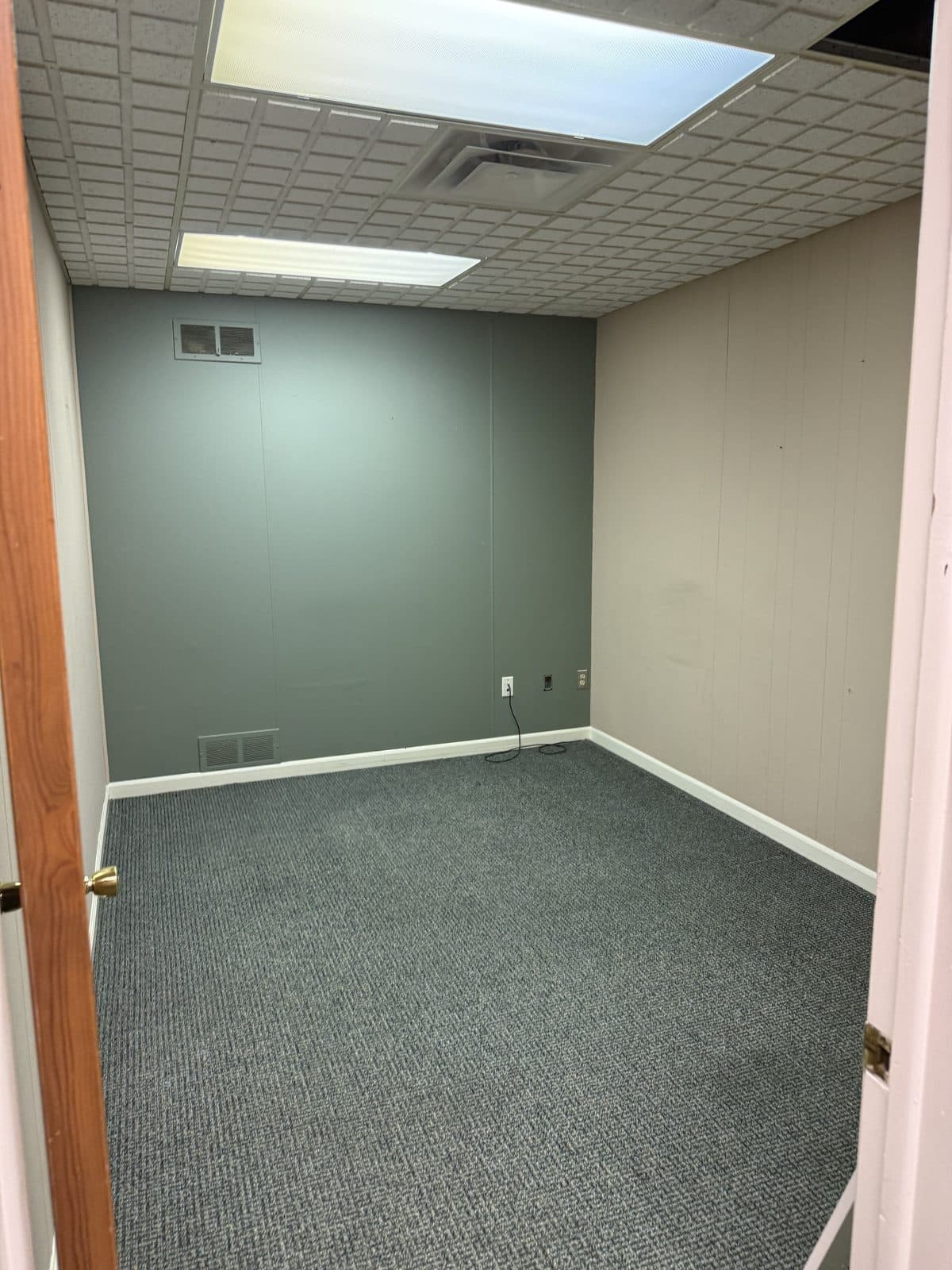 A private office with painted paneling, a wall vent, and carpet, before the interior was torn out.